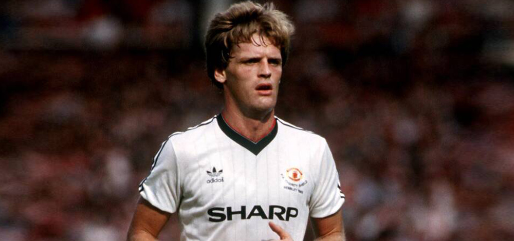 Gordon McQueen playing in a white away Manchester United kit in a full stadium